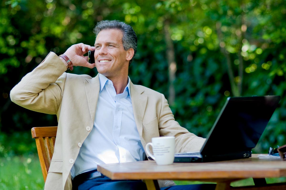 A businessman sitting outdoors talking on a mobile phone.