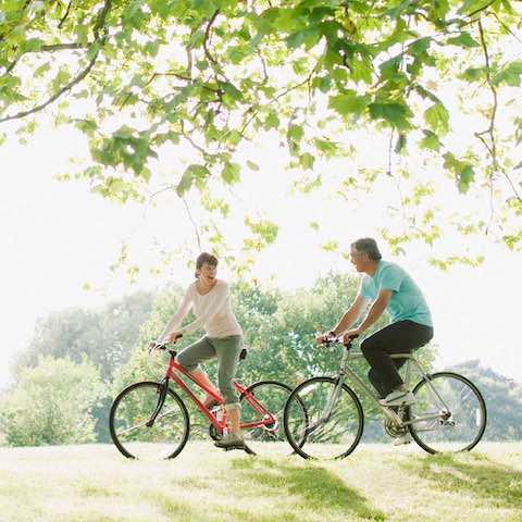 An active couple riding bicycles on a shaded greenway, enjoying the outdoors on a sunny afternoon.